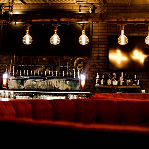 Drake's Yoke bar with industrial lighting, beer taps, liquor bottles, and a red velvet booth.