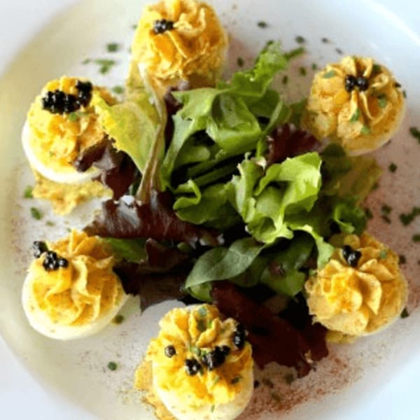 Deviled eggs topped with black caviar and chives, served with a side salad on a white plate.
