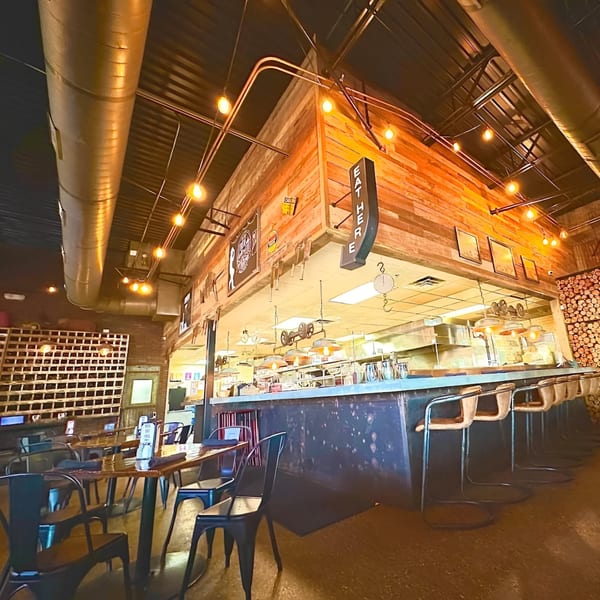 Drake's Yoke BBQ restaurant interior with industrial lighting, wooden accents, and a long bar with stools.