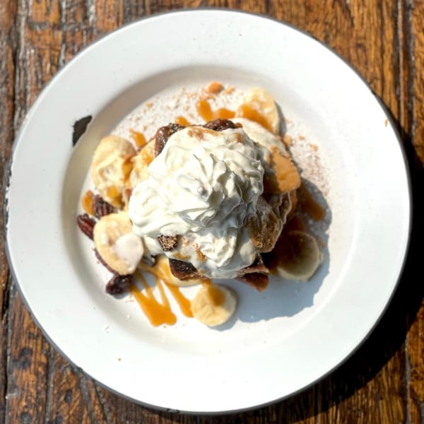 Drake's Yoke banana pudding dessert with whipped cream, caramel, and nuts on a white plate.