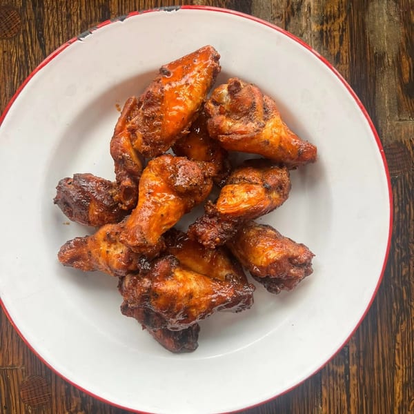 A white plate with a red rim holds a pile of glistening, saucy BBQ chicken wings.