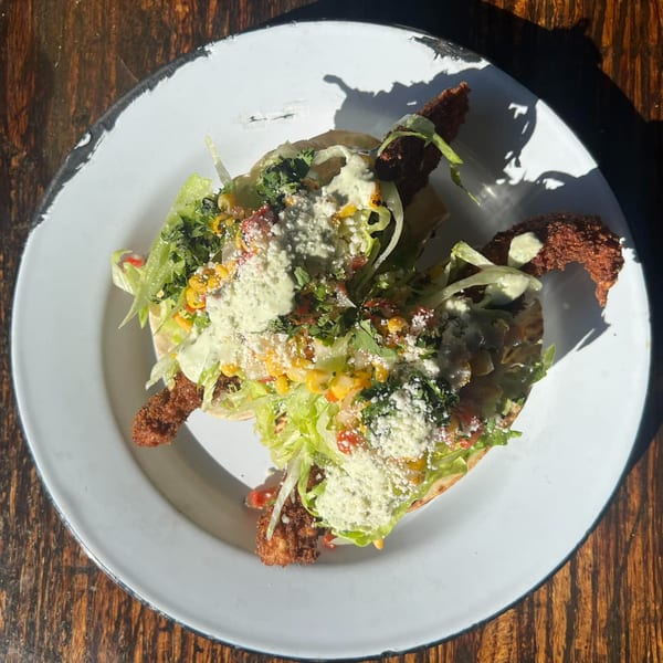Two crispy tacos topped with lettuce, corn, salsa, cotija cheese, and a creamy green sauce.