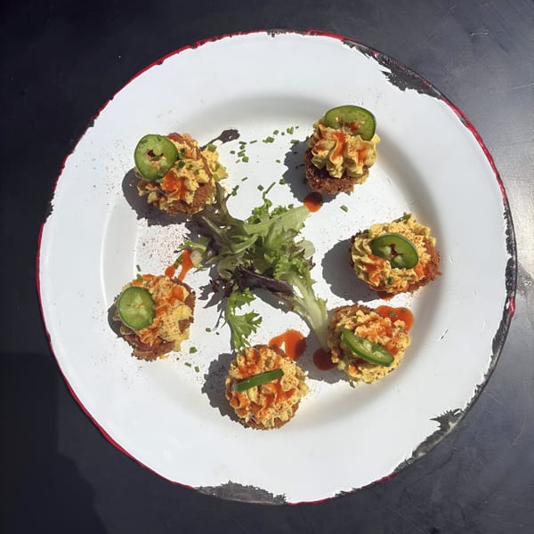 Six deviled eggs, topped with jalapeños and hot sauce, arranged on a white plate with a red rim.
